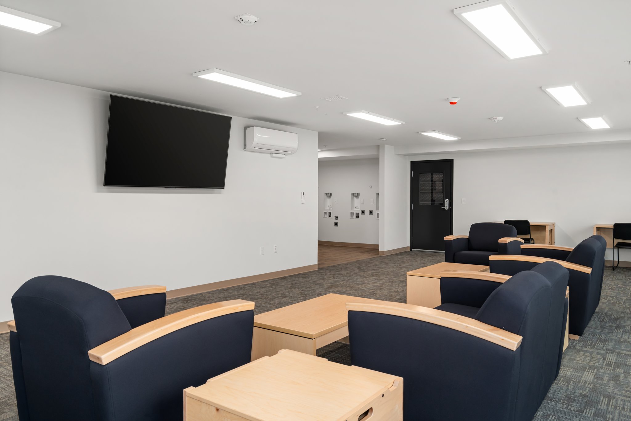 Community room with large, cushioned, blue chairs and 75-inch TV.