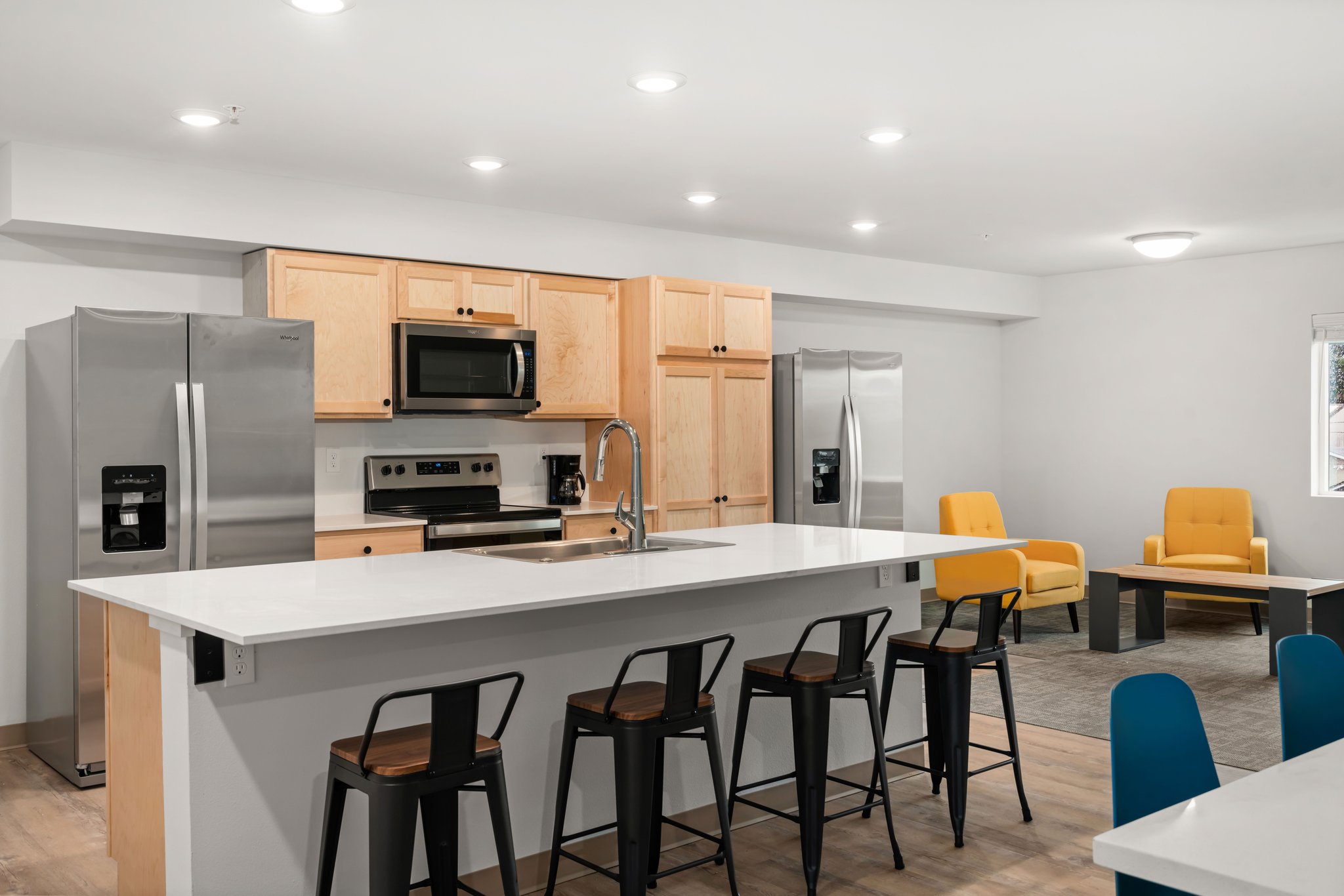 View of common room kitchen showing barstool seating at island with sink.