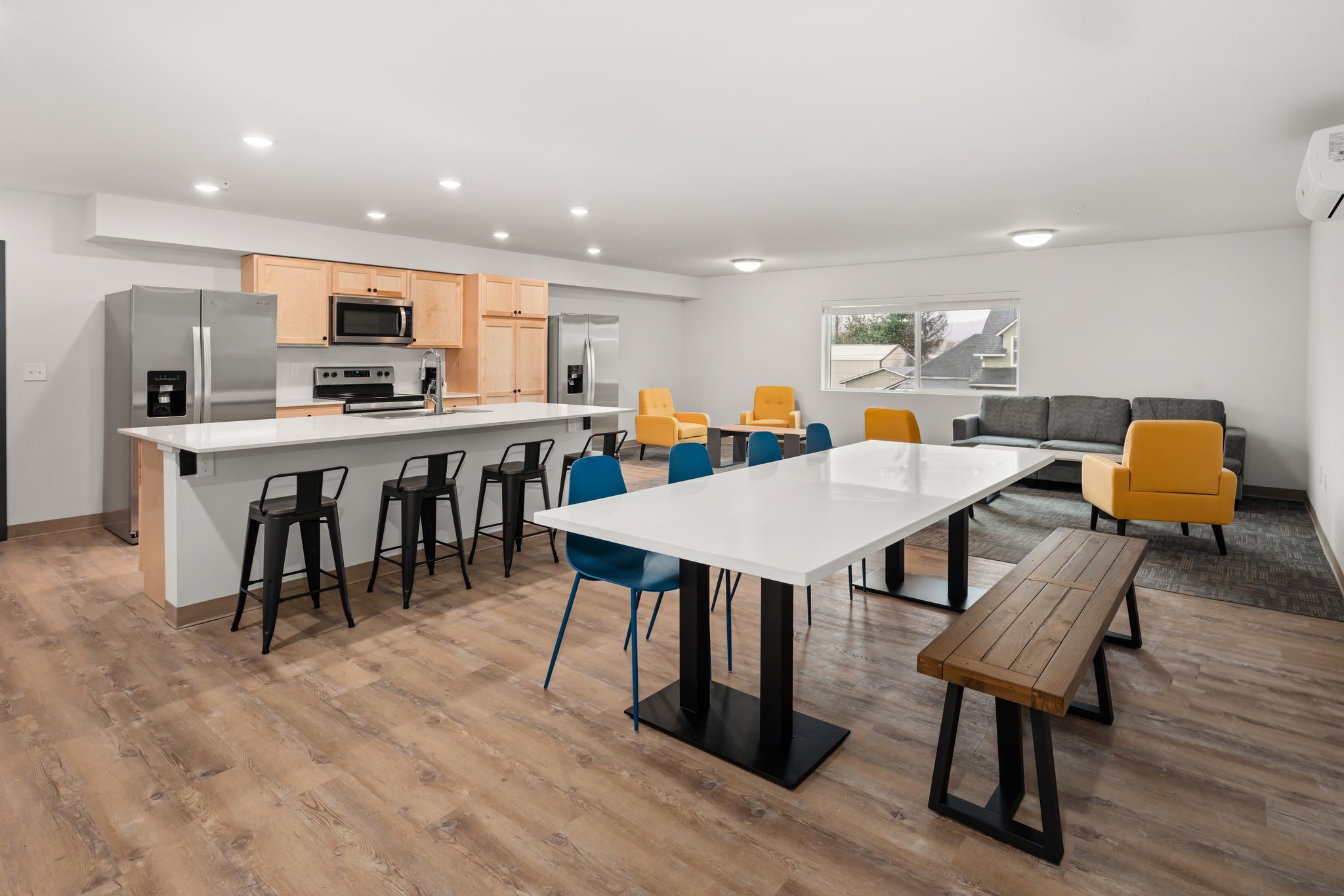 Wide view of common room showing kitchen and dining table with seating for eight.